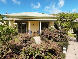 a yellow house with a porch and some bushes at Clive Colonial Cottages in Clive