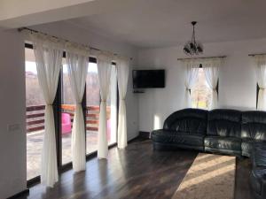 a living room with a black leather couch and windows at Popasul din Pietrar in Preluca Veche
