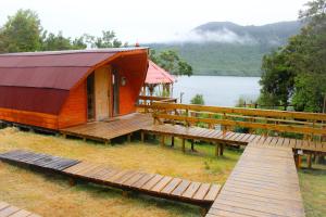 a large wooden cabin with a deck and a lake at Eco Cabañas Wanderlust in Puerto Puyuhuapi