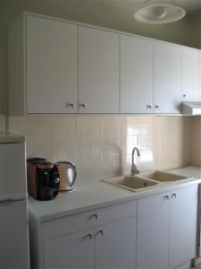 a kitchen with white cabinets and a sink and a refrigerator at Corina Apartments in Sitia