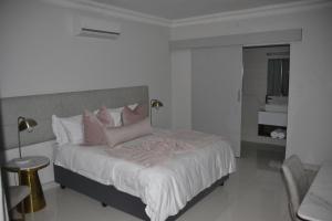 a white bedroom with a large bed with pink pillows at Prisatt Boutique Hotel in Onverwacht