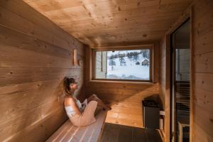 una mujer se sienta en el interior de una cabaña de madera mirando por la ventana en Rotwandwiesen Chalets SKI IN/OUT - 1900mt en Sesto
