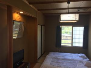 1 dormitorio con 1 cama, TV y ventana en Daymaruya Ryokan, en Yamanouchi