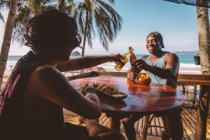 zwei Leute sitzen an einem Tisch am Strand und trinken Bier in der Unterkunft Mad Monkey Hostel Nacpan Beach in El Nido