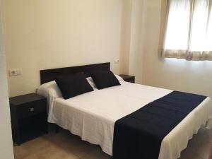 1 dormitorio con 1 cama grande con sábanas blancas y almohadas negras en Apartamentos Doña Carmen 3000, en Oropesa del Mar