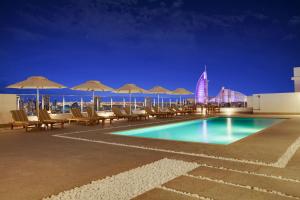 a swimming pool with chairs and umbrellas and a building at Lemon Tree Hotel, Jumeirah Dubai in Dubai