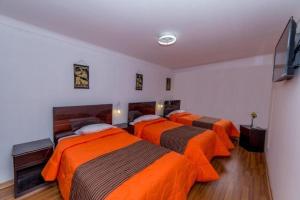 three beds in a room with orange sheets at Hotel Peru Real in Cusco