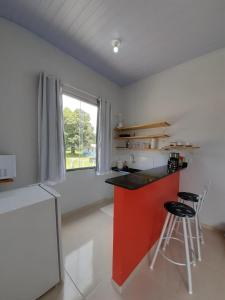 a kitchen with a red counter and two stools at Chalés Aconchego in Cavalcante