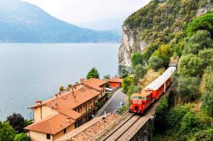a train on the tracks next to a building and water at Alice’s House in Fonteno
