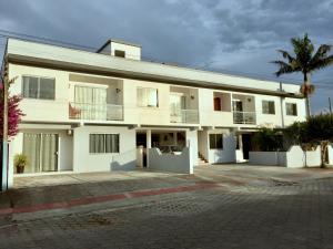 a white building with a palm tree in front of it at Residencial Sandini Garopaba in Garopaba