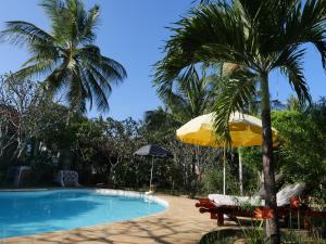 een zwembad met een palmboom en een parasol bij Frangipani Cottages in Diani Beach