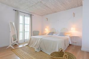 a white bedroom with a large bed in a room with windows at Can Beia Hostal Boutique in San Antonio
