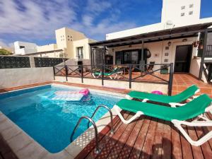 una piscina con 2 sillas de césped y una casa en Paradise Villa, en Corralejo