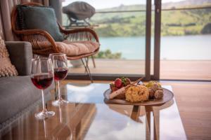 a table with a plate of food and two glasses of wine at Treetop Retreat - Takamatua Holiday Home in Takamatua Bay