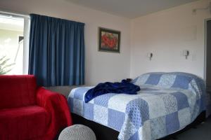 a bedroom with a bed and a red chair at Hibiscus Bed & Breakfast in Waihi Beach