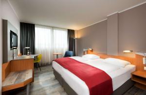 Ramada by Wyndham Hannover في هانوفر: غرفة فندق بسرير كبير مع بطانية حمراء