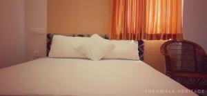 un lit avec des oreillers blancs et une chaise dans une chambre dans l'établissement Thenmala Heritage, à Kollam