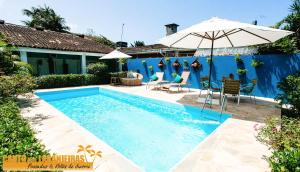 Una piscina con sillas y una sombrilla al lado de una casa. en Canto das Laranjeiras Villa, en Guarujá