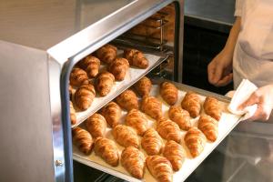 a baker is putting a tray of croissants in an oven at Ark Hotel Royal Fukuoka Tenjin -ROUTE INN HOTELS- in Fukuoka