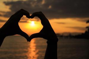 a pair of hands making a heart shape with the sunset in the background at Minu Hotel in Fethiye