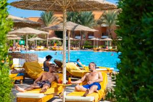 twee mannen zitten op ligstoelen bij het zwembad van het resort bij Three Corners Sunny Beach Resort in Hurghada