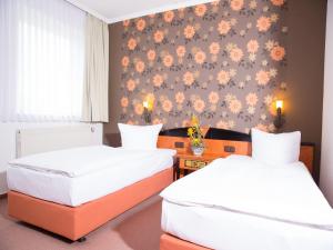 two beds in a room with a wall with flowers at Pension Weinberg Güstrow in Güstrow