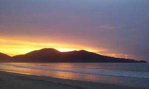 een zonsondergang boven een strand met bergen op de achtergrond bij Ubatuba Surf Hostel, apenas a 60 metros da praia da Lagoinha! in Ubatuba