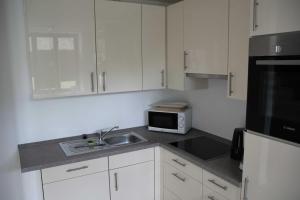 eine Küche mit weißen Schränken, einer Spüle und einer Mikrowelle in der Unterkunft Strandresidenz Appartement Kormoran A07 in Binz