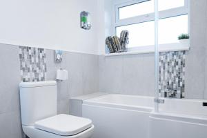 a white bathroom with a toilet and a tub and a window at The Duplex Margate with Deck & Living Space Air Conditioning in Margate +37 photos