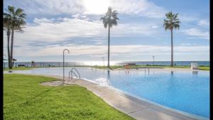 a swimming pool with palm trees and the ocean at MI CAPRICHO A17 Beachfront Apartment in La Cala de Mijas