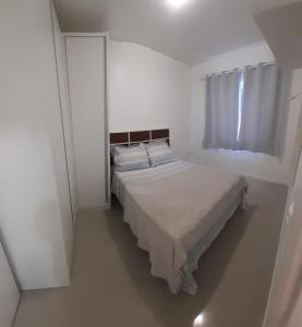 Cama en habitación blanca con ventana en Apartamento 2 dormitório praia de Bombas, en Bombinhas