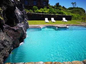 - une piscine avec 2 chaises longues et un mur de roche dans l'établissement Hotel os Moinhos, à Velas