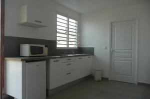 a white kitchen with a microwave and a sink at Douceurs Caraïbes, Gîte Coco. in Bouillante