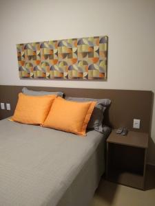 a bed with an orange pillow and a painting on the wall at Rio Quente Flat Veredas Apto - 231 in Rio Quente