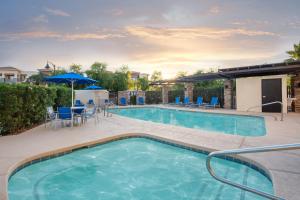 a swimming pool with chairs and a table and an umbrella at Holiday Inn Express Surprise by IHG in Surprise