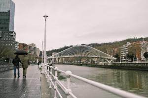 two people walking on a bridge with an umbrella at ZUBIGANE apartamento junto a la Ría & Parking in Bilbao