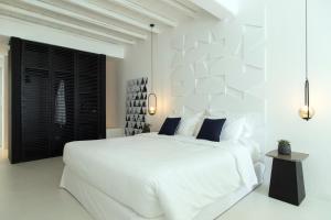 a white bedroom with a large white bed with blue pillows at Nimbus Mykonos in Agios Stefanos