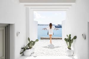 a woman walking into a white room with a view of the ocean at Nimbus Mykonos in Agios Stefanos
