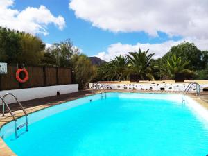 a large blue swimming pool with chairs and trees at Rural Rugama in Puerto del Rosario