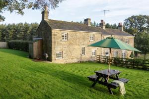 una mesa de picnic con una sombrilla delante de una casa en Carr Cottage en Leeds