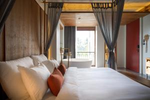 a bedroom with a large white bed with a window at Hotel Gahn Khao Lak in Khao Lak