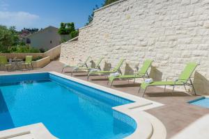 a swimming pool with green chairs and a brick wall at Villa Kogo in Hvar
