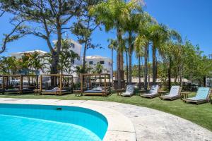 a pool at a resort with lounge chairs and palm trees at Selina Floripa in Florianópolis