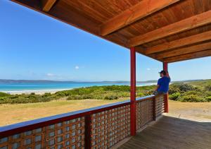 una persona parada en un porche con vistas al océano en Cloudy Bay Cabin, en South Bruny