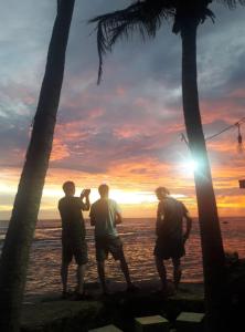 Malee Villa (Beach Inns Holiday Resort) في ماتارا: ثلاثة رجال واقفين على الشاطئ ينظرون إلى غروب الشمس