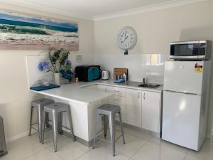 a white kitchen with a white refrigerator and stools at Lazy Dayz Shellharbour in Shellharbour