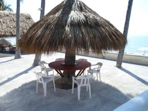 una mesa y sillas bajo una sombrilla de paja en la playa en Bucerias Beach House, en Bucerías