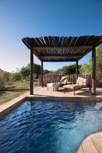 a swimming pool with a wooden pergola and a patio at Kwandwe Great Fish River Lodge in Grahamstown