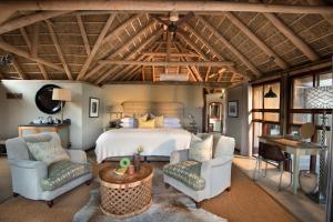 a bedroom with a bed and two chairs and a table at Kwandwe Great Fish River Lodge in Grahamstown