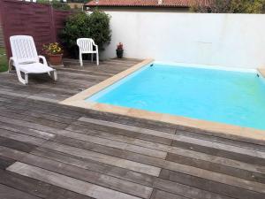 a swimming pool with two chairs on a wooden deck at Les Hirondelles in Puyoô